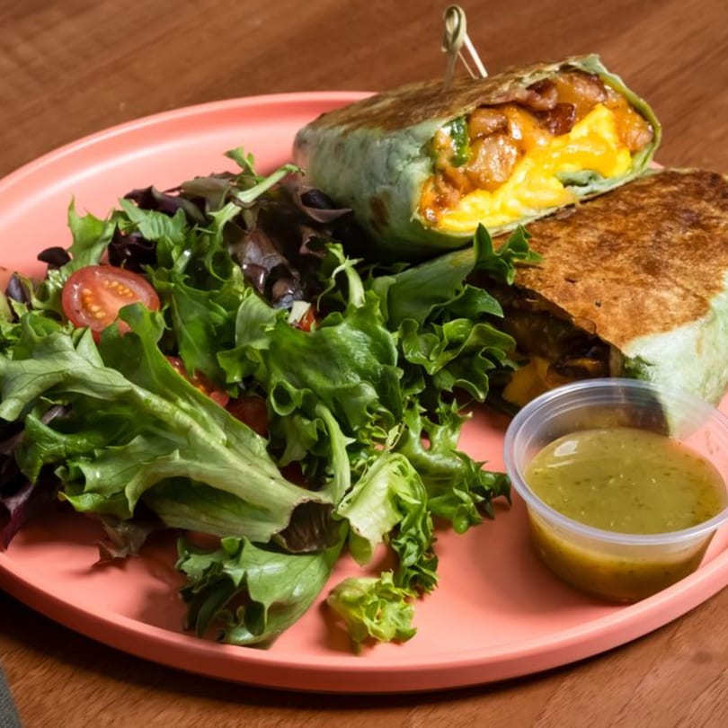 Breakfast burrito with scrambled eggs, bacon, and cheese, served with a side salad and green dressing.