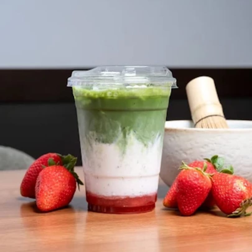 Strawberry matcha latte in a clear cup with fresh strawberries and a matcha whisk.