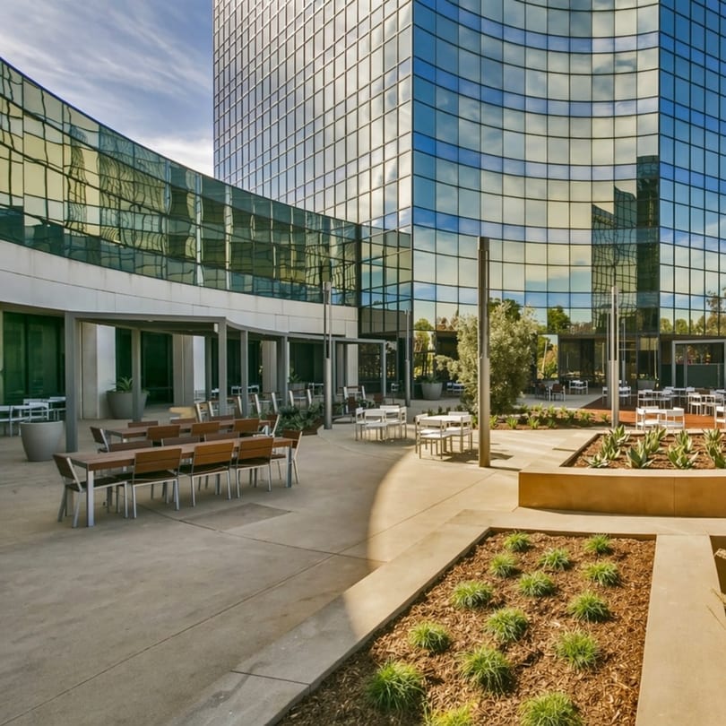 Outdoor patio with tables and chairs in front of a modern glass building with reflections.