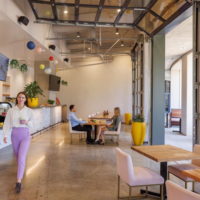 A woman walks past a cafe counter while two people dine at a table in a modern restaurant.
